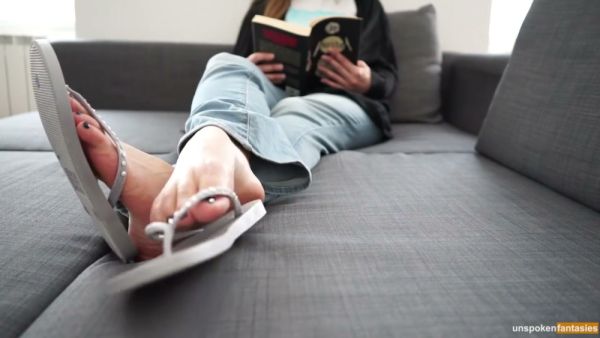 POV foot fetish scene with bare soles in focus while someone reads on the couch on breastful.com