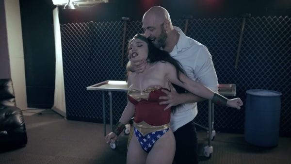 Brunette in Wonder Woman costume dominated in a shadowy institutional chamber on breastful.com