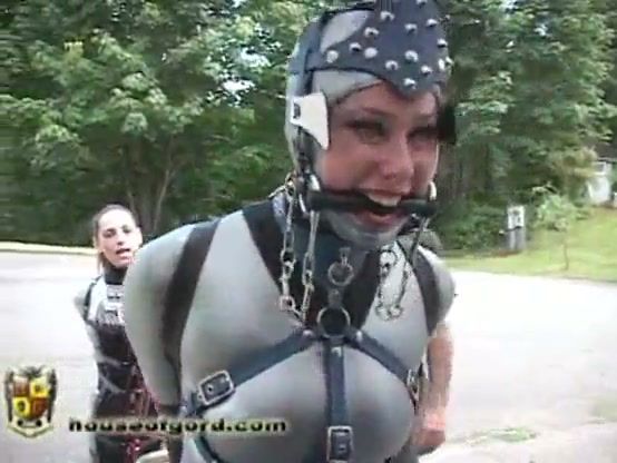 Latex-clad submissive trained with a red cart in outdoor bondage session on breastful.com