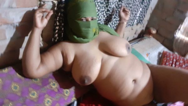 Full-figured woman in a mysterious green mask teases beneath patterned blankets on breastful.com