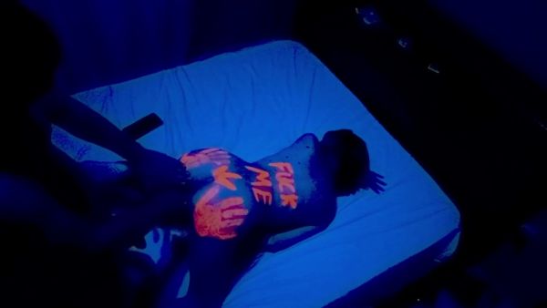 Latina couple glows under blue light with neon handprints during intimate night filming on breastful.com