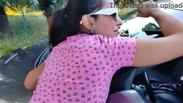 Young woman in pink dress gives bold outdoor blowjob beside a car while someone watches on breastful.com