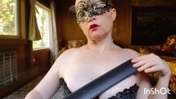 Strict dominatrix in black corset and mask disciplines with paddle and flogger on breastful.com