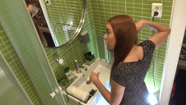 Blonde woman adjusts her hair in front of the bathroom mirror wearing a black floral dress - Usa on breastful.com