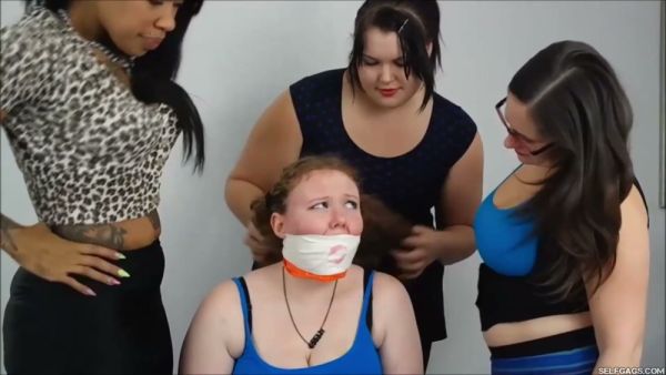 Red-haired woman subdued and gagged by three dominant women in a white room on breastful.com