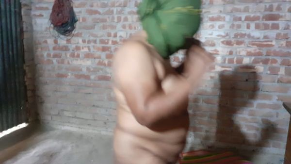 Nude figure in a brick room adjusts green headcloth under dim light on breastful.com